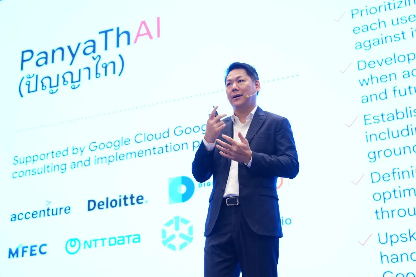 A speaker on stage beside a PanyaThAI slide listing the programme's consulting and implementation partners, among them Digithun Worldwide, Accenture, Deloitte, MFEC and NTT DATA.
